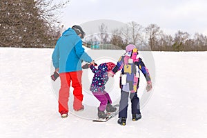 Winter extreme sport. Father and daughter are teaching kid sister snowboarding on a snow slope