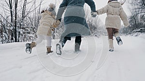 winter family activity outdoors. back view. Happy woman with 2 daughters are running on snowy road, in forest, during