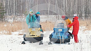 Winter. A family in colorful jackets are getting on snowmobiles and ready for the ride