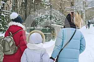 Winter family walk in the city, the mother and her daughters walk along the snow-covered city street, the view from the back