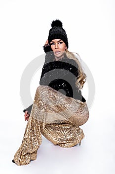 Winter fashion. Beautiful young blonde woman in winter sequin outfit and beanie isolated on white background in studio. The model