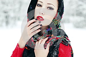 Winter fashion concept. Portrait of young woman in red cardigan and russian kerchief posing in the park. Snowflakes on lashes.