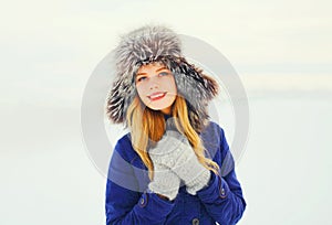 Winter fashion portrait happy smiling woman wearing fur hat over snow