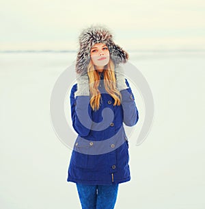 Winter fashion portrait smiling woman wearing fur hat over snow