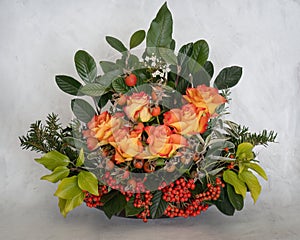 Winter festive floral arrangement. Flame colour roses, berries, greenery and leaves. On pale background.