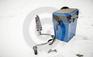 Winter fishing. Blue plastic fishing box and ice drill in the snow