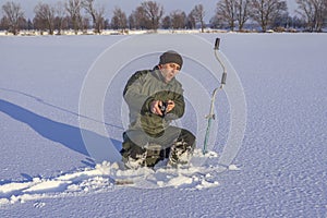 Winter fishing concept. Fisherman in action. Catching fish from snowy ice.