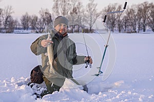 Winter fishing concept. Fisherman in action with trophy in hand. Catching pike fish from snowy ice at lake.