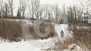 Winter fishing concept. Fisherman with professional equipment and ice drill is walking on snow at frozen lake