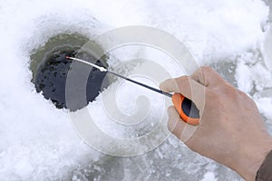 Winter fishing concept. Hand of fisherman with specialised rod above snowy ice