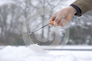 Winter fishing concept. Hand of fisherman with specialised rod above snowy ice