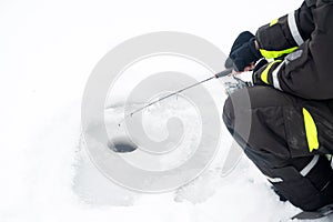 Winter fishing on ice. Man jiggling bait in an ice hole. Relaxing in the wild