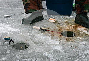 Winter fishing rods lie on holes drilled in the ice near the feet of the fisherman.