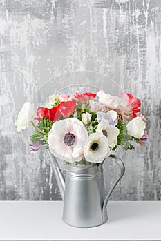 Winter flowers. Anemones in a vase watering can standing on a wooden table. On the background old gray wall art. copy