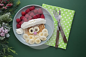 Winter food for kids. Christmas Santa pancake with raspberry and banana for children menu, green background, copy space