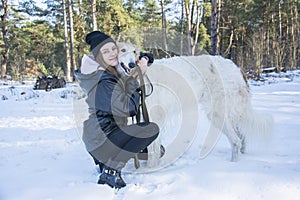 In the winter forest on a bright sunny day, a girl hugs a Russian greyhound dog