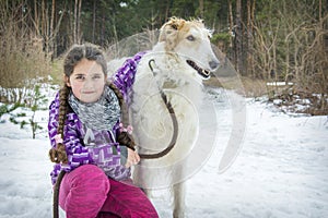 In the winter forest on a bright sunny day, a girl hugs a Russian greyhound dog