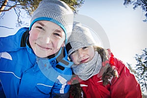 In winter, in the forest on a bright sunny day, happy brother and sister are standing in an embrace