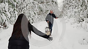 In the winter forest, the girl stands with her back with her hands open, and a man with a husky dog runs to meet her. A