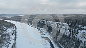 Winter forest landscape and pine tree forest growing on cliff over frozen river in snow. Clip. Breathtaking aerial view