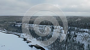 Winter forest landscape and pine tree forest growing on cliff over frozen river in snow. Clip. Breathtaking aerial view