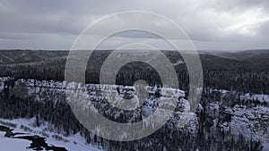 Winter forest landscape and pine tree forest growing on cliff over frozen river in snow. Clip. Breathtaking aerial view