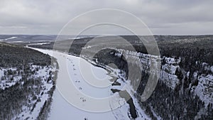 Winter forest landscape and pine tree forest growing on cliff over frozen river in snow. Clip. Breathtaking aerial view