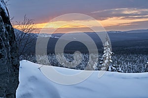 Winter forest with snow-covered fir trees high in the mountains. Dawn with bright colors on the horizon far away in the mountains