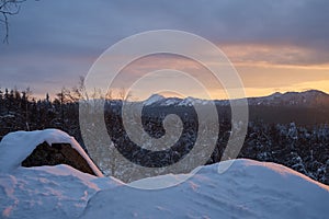 Winter forest with snow-covered fir trees high in the mountains. Dawn with bright colors on the horizon far away in the mountains