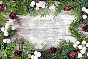 Winter frame with evergreen branches, white berries and pine cones on a white wood banner background photo