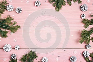 Winter frame of fir branches, cones and stars on pink wooden background