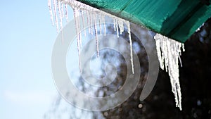 Winter, frosty, snowy, sunny day. close-up, large transparent icicles hang from the roof, against the sky.