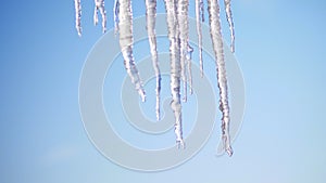 Winter, frosty, snowy, sunny day. close-up, large transparent icicles hang from the roof, against the sky.