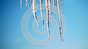 winter, frosty, snowy, sunny day. close-up, large transparent icicles hang from the roof, against the sky.