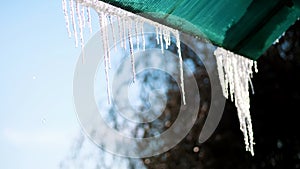 winter, frosty, snowy, sunny day. close-up, large transparent icicles hang from the roof, against the sky.