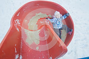 Winter fun of little girl on red plastic playground slide