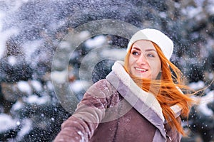 Winter ginger redhead girl throwing snowball at camera smiling happy having fun outdoors on snowing winter day playing in snow