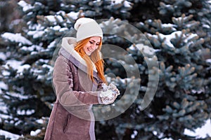 Winter ginger redhead girl throwing snowball at camera smiling happy having fun outdoors on snowing winter day playing in snow