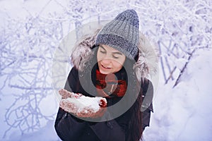 Winter girl in red gloves and scarf blowing snow. Beauty Joyful Teenage Model Girl having fun in winter park. Beautiful girl laugh