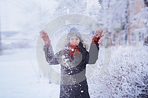 Winter girl in red gloves and scarf blowing snow. Beauty Joyful Teenage Model Girl having fun in winter park. Beautiful girl laugh