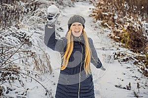 Winter girl throwing snowball at camera smiling happy having fun outdoors on snowing winter day playing in snow. Cute