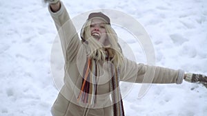 Winter girl throwing snowball at camera smiling happy having fun outdoors on snowing winter day playing in snow. Cute