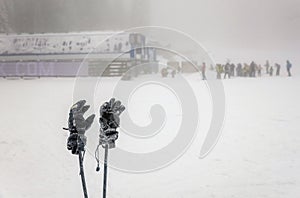 Winter gloves and skii poles with people skiing on extreme weather with fog in the background