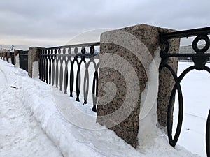 winter, granite pillar and cast iron embankment fence in the snow