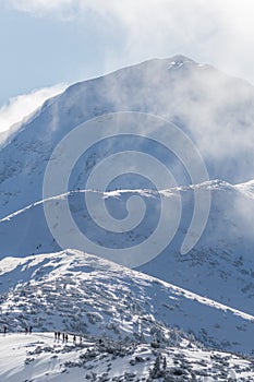 Winter hiking in West Tatras. Popular trail with many tourists during sunny day. Volovec peak in background.