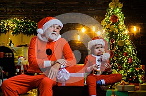 Winter holiday. Christmas decoration. Santa Claus with little helper near Christmas tree. Santa man and funny child boy