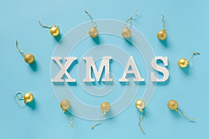 Winter holiday composition. Text Xmas from white letters and christmas decoration golden balls on blue background