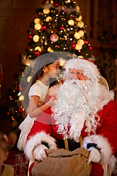 Winter holiday concept - girl telling wish Santa Claus