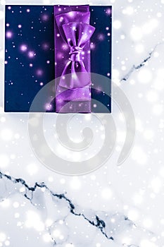 Winter holiday gift box with purple silk bow, snow glitter on marble background as Christmas and New Years presents for luxury
