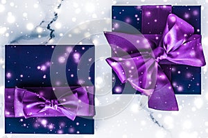 Winter holiday gift box with purple silk bow, snow glitter on marble background as Christmas and New Years presents for luxury